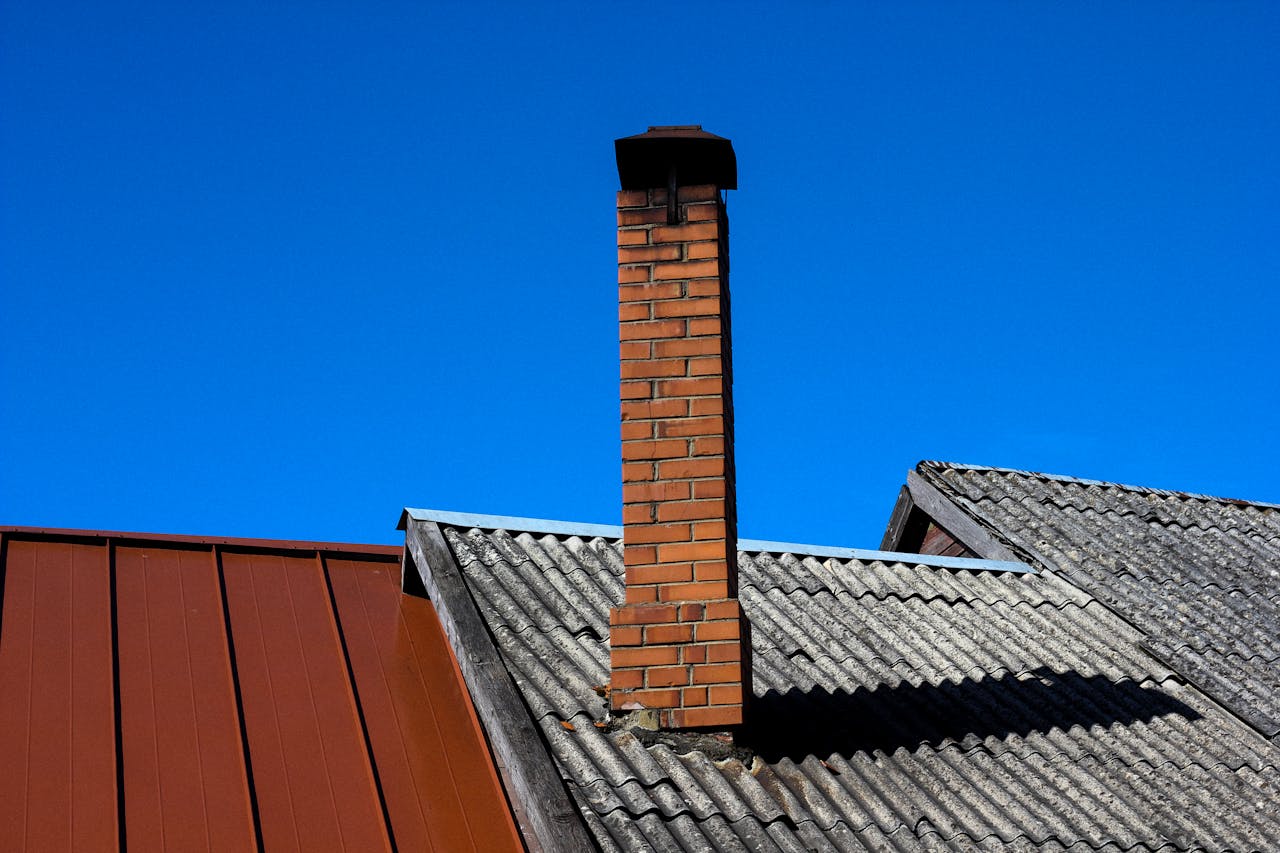 about-us A solitary brick chimney rises from a tiled roof under a vibrant blue sky, showcasing minimal architecture.